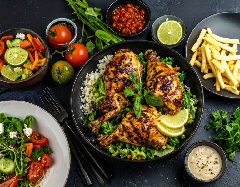 Hähnchen und Gemüse schön angerichtet mit einem Reis-Gemüsebett. Daneben sind fettfreie Pommes, Salsa, Tomaten, Salat und Dip zu sehen, symbolisiert die Art des Kochens vom Privatkoch für Sportler.